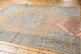 Distressed Turkish Oushak rug corner with worn pile, pale peach, and faded blue floral motifs.