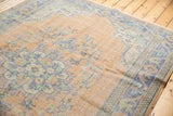 Distressed Oushak carpet corner; pale peach field, faded blue and mint floral motifs, visible wear.
