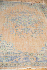 Distressed vintage Oushak rug showing worn pile, faint foundation, and faded peach, blue florals.