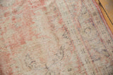 Distressed vintage Oushak carpet's worn texture, featuring faded blush rose and cotton white, with faint motifs.