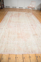 Distressed vintage Oushak carpet with prominent worn texture and blush rose on cotton white.