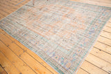 Distressed Oushak rug corner showing faded mint, blue, apricot border with foundation.