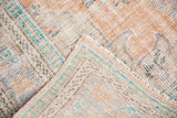 Distressed texture and faded tones of a vintage Oushak rug, showing secured edge and foundation.