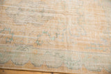 Distressed Oushak carpet's scalloped border with visible foundation, in apricot gold and seafoam green.