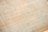 Close-up of distressed Oushak rug, showing muted ivory, apricot, and faded mint pattern with visible foundation.