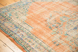 Distressed Oushak rug corner, showing exposed foundation and worn floral motifs in blush and faded blue.