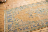 Vintage distressed Oushak carpet with faded golden field and hints of blue and green floral motifs.