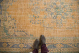 Feet on distressed vintage Oushak carpet, showing worn pile, blush, and faded blue motifs.