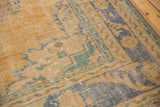 Distressed Oushak carpet border detail: faded gold, muted teal, blue patterns, visible wear.