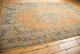 Distressed Oushak rug with a faded golden field, worn pile, and blue-green floral motifs.