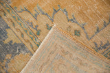 Distressed Oushak rug corner revealing worn pile, faded blue, gold tones, and woven foundation.