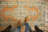 Faded burnt orange, ivory, and seafoam geometric medallion on a distressed Oushak runner.