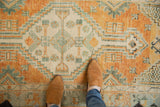 Distressed Oushak runner texture with faded orange, ivory, and seafoam green geometric patterns.