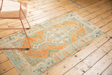 Corner of distressed Oushak runner with faded orange, ivory, and seafoam green geometric motifs.