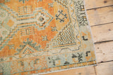 Distressed Oushak rug corner with faded orange, seafoam green, and ivory geometric patterns.