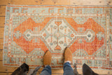 Distressed Oushak corner with germinating seed motif in cinnabar red, ivory, and slate blue.