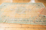 Distressed vintage Oushak rug showing worn apricot field and faded blue-green border motifs.