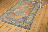 Distressed vintage Oushak rug corner with terracotta, faded blue, and gold floral border.