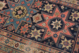 Intricate star and geometric motifs in dusty blush, navy, and gold on an antique Shirvan rug.