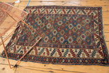 Antique Shirvan rug corner, showing mallard green field, geometric border, and tattered fringe.