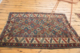 Bottom corner of Antique Shirvan rug, showing geometric border of serrated leaves in wine red, ivory, and blue. Tattered edge.