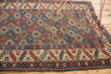 Geometric border and gul motifs on an antique Shirvan rug, showing even wear and tattered edge.