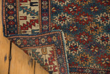 Antique Shirvan rug corner: mallard green gul pattern, geometric border, and tattered selvage.