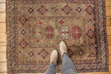 Antique Caucasian rug's detailed central octagonal medallions and geometric guls in bronze, wine, and ivory.