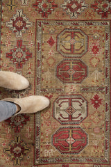 Geometric rust red guls, ivory people motifs, and intricate border on antique Caucasian rug.