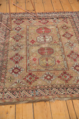 Corner of antique Caucasian rug, featuring geometric guls, intricate borders, and worn fringe.