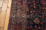Meshed carpet navy field, wine border, scrolling floral tendrils, visible wear.