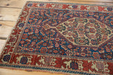 Corner of antique Persian Senneh rug, showing worn Herati motif in navy, wine red, and ivory.