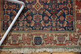 Antique Senneh rug border featuring ivory, wine red motifs, navy field, and tattered fringe.