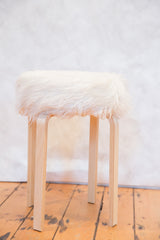 White faux fur top detail and curved light wood legs of the Alvar Aalto style stool.