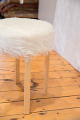Fluffy white faux fur texture of the stool's seat meeting light wooden legs.