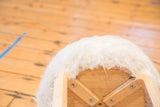 Light wood base structure of an Alvar Aalto style stool with white faux fur.