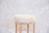 Fluffy white faux fur and curved wood legs of the Alvar Aalto style stool.