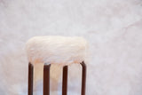 Fluffy white faux fur on curved dark wood Alvar Aalto style stool.