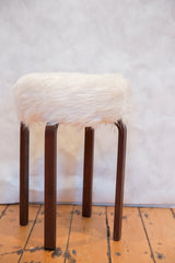 Furry white top and curved dark wood legs of a unique Alvar Aalto style stool.