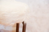 Fluffy ivory faux fur top texture meeting the dark wooden legs of the Aalto style stool.