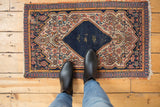 Upper corner of vintage Senneh rug with navy border, beige Herati motif, and tattered edge.