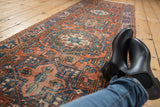 Dusty brick red Heriz runner with navy geometric motifs and visible soft wear.