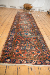 Vintage Heriz runner's geometric and curvilinear motifs, brick red field, and navy serrated border.
