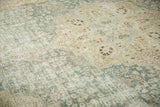 Distressed vintage Tabriz carpet texture showing muted aqua, beige, and brown floral patterns.