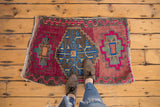 Vintage distressed Oushak rug featuring bright blue medallion on cranberry, pink, and grey field.