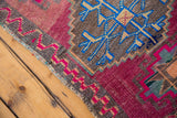 Distressed vintage Oushak rug showcasing geometric blue motifs, pink zigzags, and selvage.