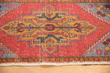 Distressed Oushak rug close-up: faded brick red field, elongated gold medallion, slate blue accents.