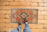 Distressed Oushak rug pile featuring worn dusty brick red and charcoal medallion.