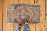 Distressed vintage Oushak rug mat showcasing a geometric medallion and faded mauve, purple, blue tones.