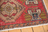 Distressed vintage Oushak rug corner, showing brick red pile, wear, and geometric border.